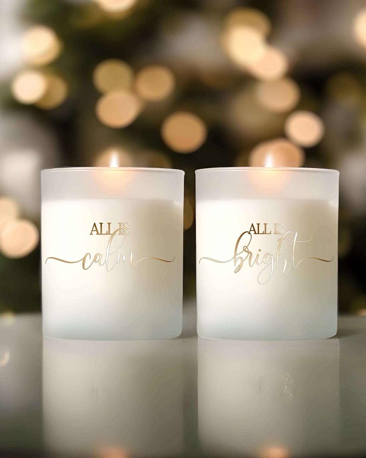 Two white candles burning brightly with gold accented words written on the front “All is calm” “All is bright”.