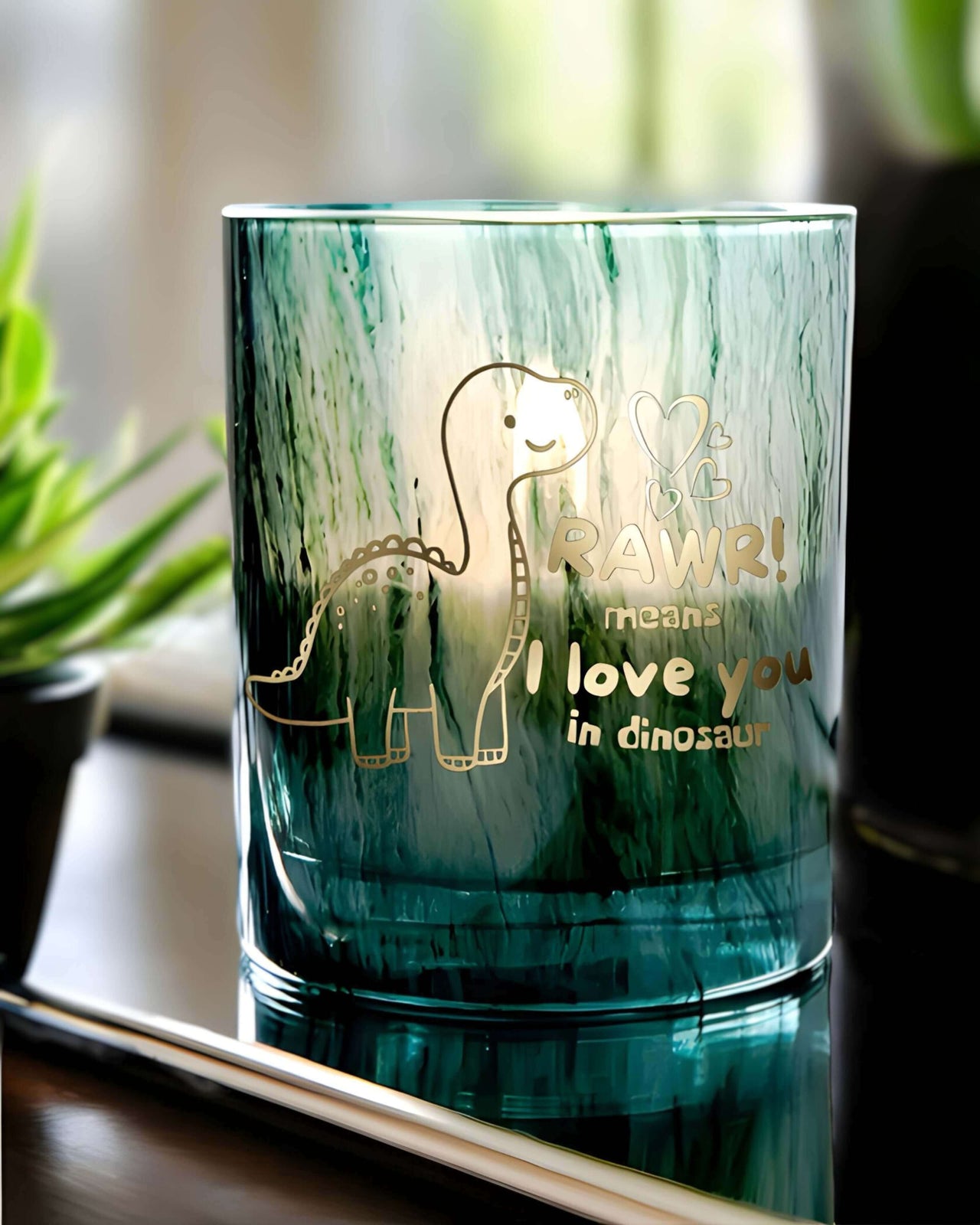 The image represents an green glass jar candle with gold writing that reads " RAWR! means i love you in dinosaur"