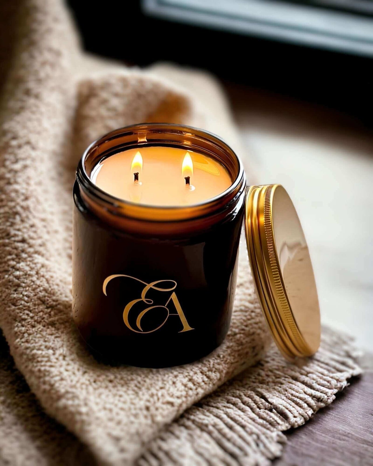 An amber glass candle sitting on a cashmere throw in a darkened room with soft light.